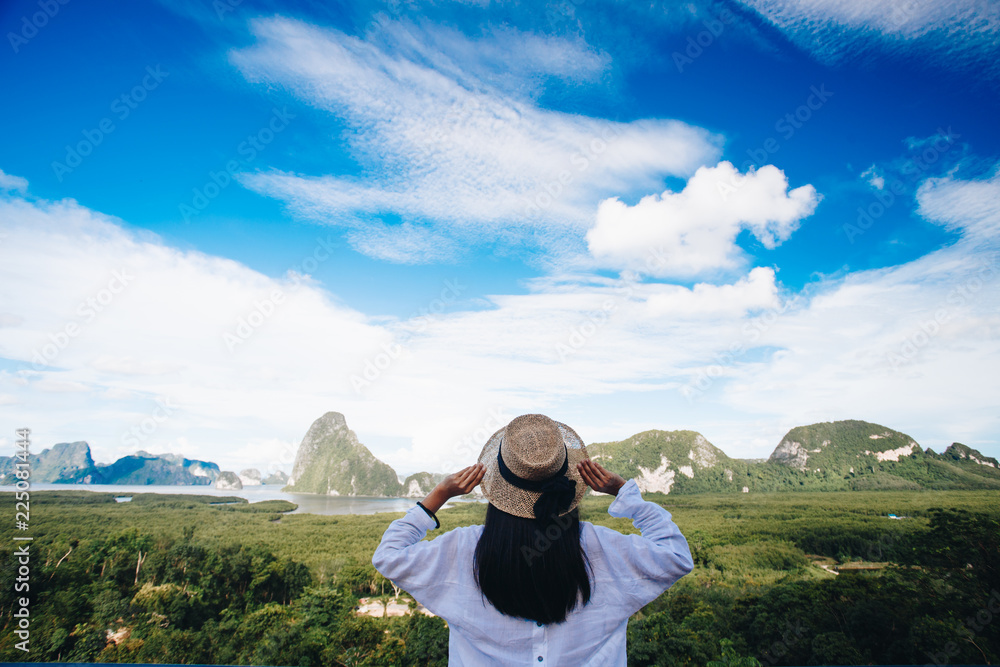 Asian woman traveler wearing a white shirt holding hat and looking at amazing mountains and forest, travel holiday relaxation concept.
