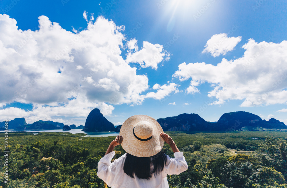Asian woman traveler wearing a white shirt holding hat and looking at Samed Nang Chee amazing mountains and forest, travel holiday relaxation concept.