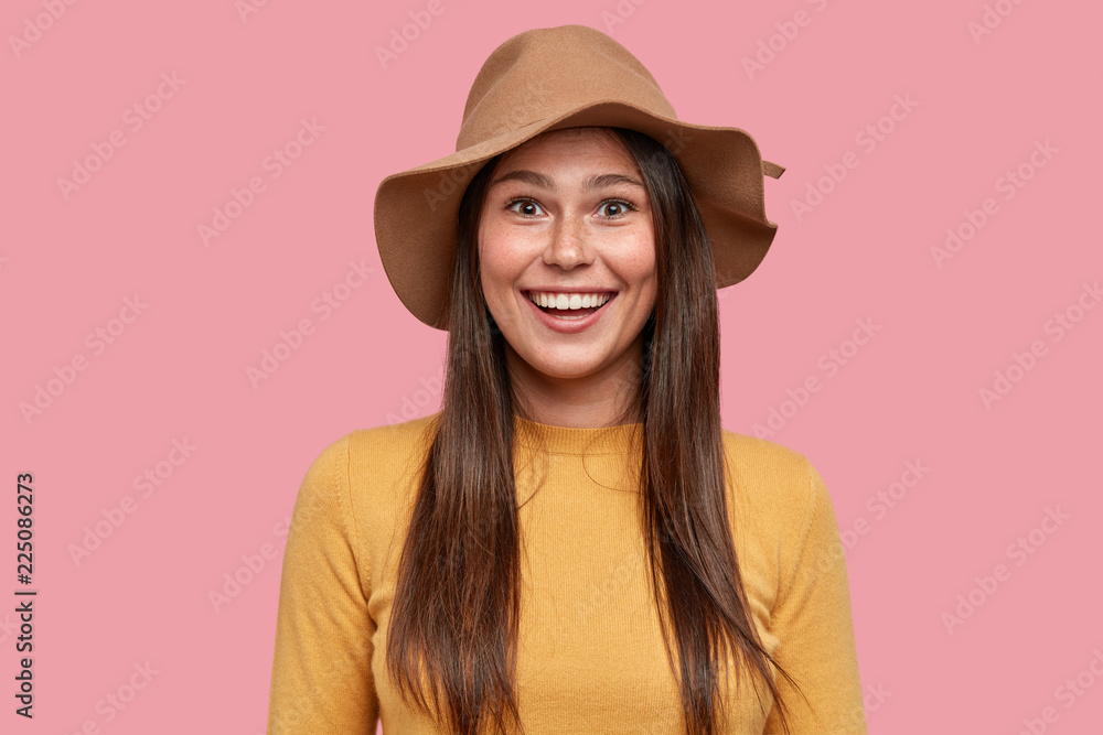 Joyful woman in romantic mood gazes with pleasant smile, rejoices relationships, wears fashionable hat and yellow clothes, isolated over pink background. People and positive emotions concept Joyful woman in romantic mood gazes with pleasant smile, rejoices relationships, wears fashionable hat and yellow clothes, isolated over pink background. People and positive emotions concept