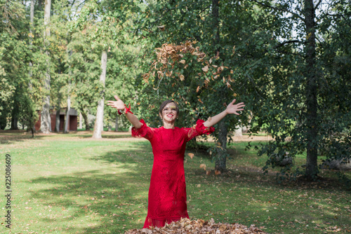 Young woman in red dress. Toss the autumn leaves upward. photo