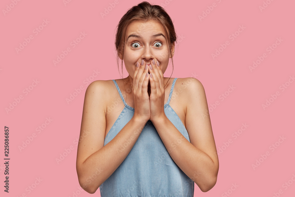 Overjoyed European dark haired woman keeps both hands on mouth, reacts on positive news, doesnt expect to win lump sum of money, expresses good emotions, cant stop laughing. Happiness concept Overjoyed European dark haired woman keeps both hands on mouth, reacts on positive news, doesnt expect to win lump sum of money, expresses good emotions, cant stop laughing. Happiness concept