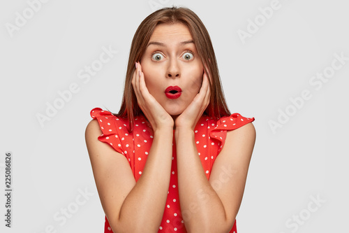 Shocked stupefied speechless brunette woman with eyes popped out, red lips, cant believe in awful news, dressed in fashionable summer dress, models against white background. Omg spring sale near.
