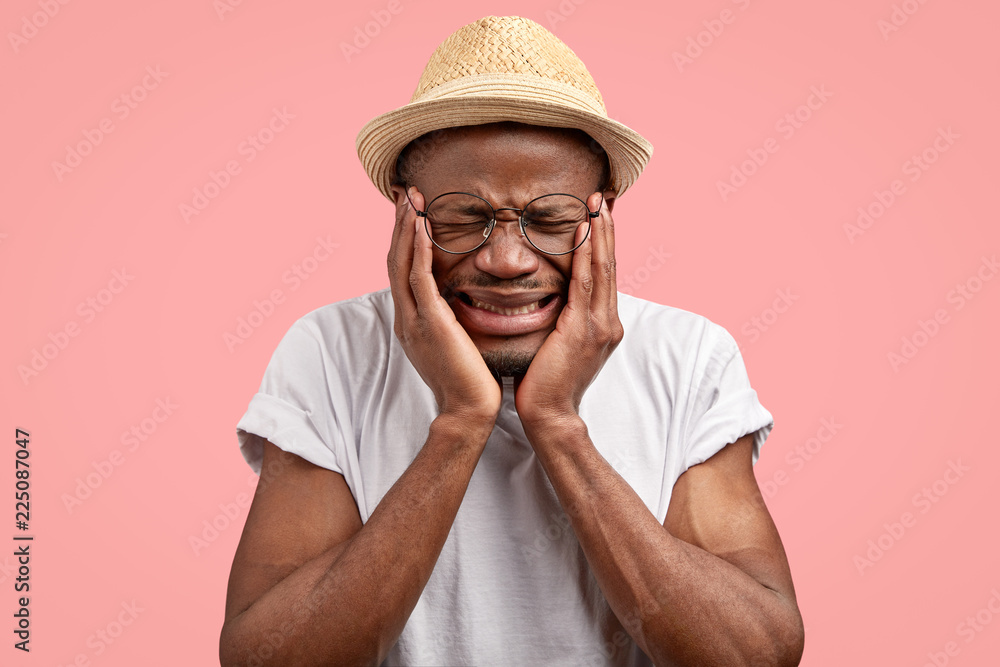 Depressed unhappy dejected man with dark skin, frowns face in discontent, feels sad as have problems in life, wears casual t shirt, poses against pink background. Negative human emotions concept Depressed unhappy dejected man with dark skin, frowns face in discontent, feels sad as have problems in life, wears casual t shirt, poses against pink background. Negative human emotions concept