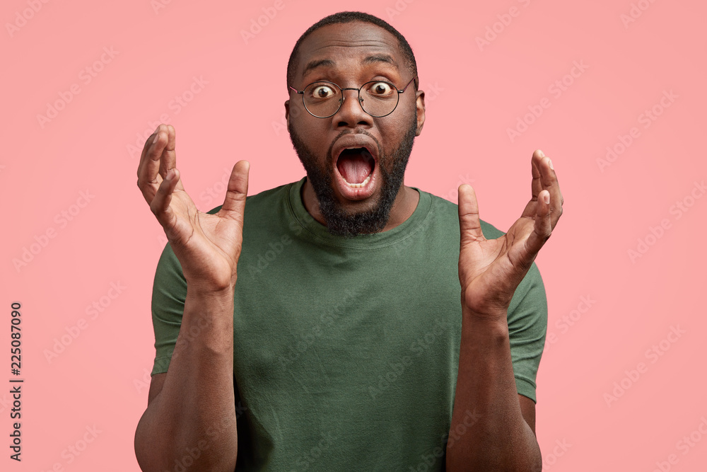 Impressed surprised black guy opens mouth widely, holds plams near face
