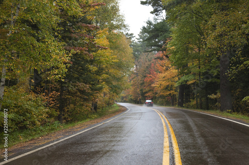 Car driving on a curving road in northern Minnesota with trees in autumn color on a rainy day