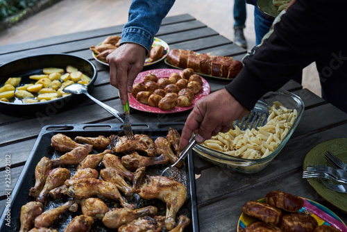Catering buffet food table with baked potatoes, fried chicken legs, pasta and vegetable salad. People at a party taking different food, outdoor. Colleagues Buffet Party Brunch Dining Concept