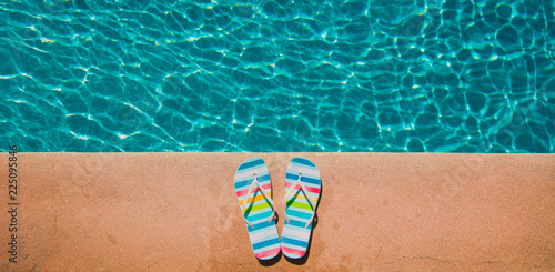 Colored summer sandals near blue pool. Above view