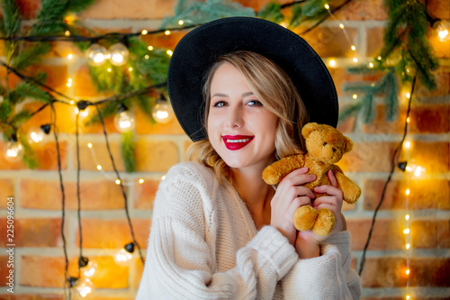 Portrait of a young cozy woman in white sweater with teddy beartoy and Christmas lights on background. photo