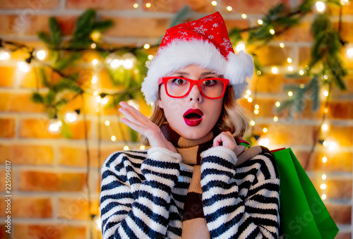 Portrait of a young cozy woman with shopping bags and Christmas lights and pine branch on background.