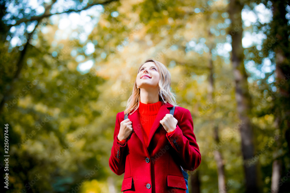 Young woman with red coat and packpack in autumn season park. Young woman with red coat and packpack in autumn season park.