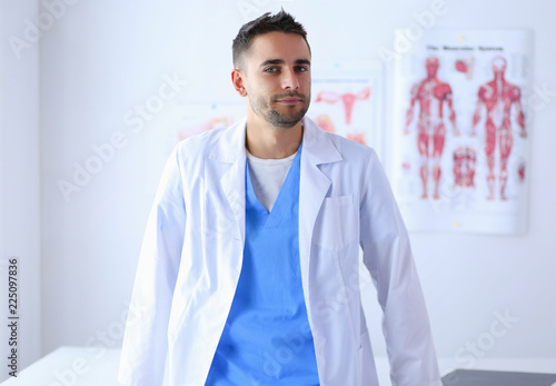 Young and confident male doctor portrait standing in medical office. photo