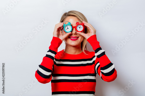 Portrait of a beautiful white smiling woman in red sweater with little alarm clocks on white background, isolated.