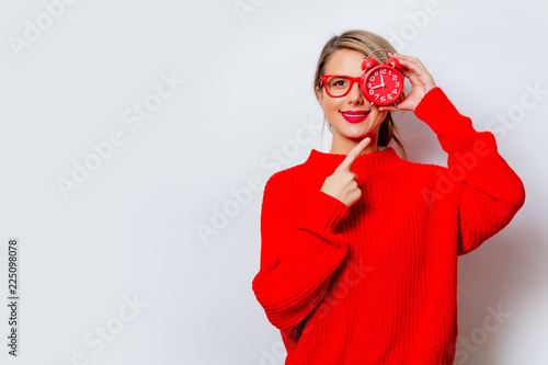 Portrait of a beautiful white smiling woman in red sweater with little alarm clock on white background, isolated.