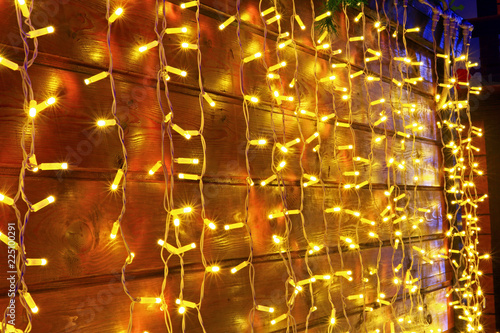 On merry or romantic holidays, a big long garland of yellow color beautifully and brightly illuminates wooden planks (wall, fence) and creates a cozy atmosphere. © ramaikina