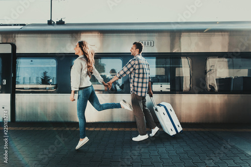 Full length side view cheerful male holding hand of young smiling lady. She jumping near him opposite train