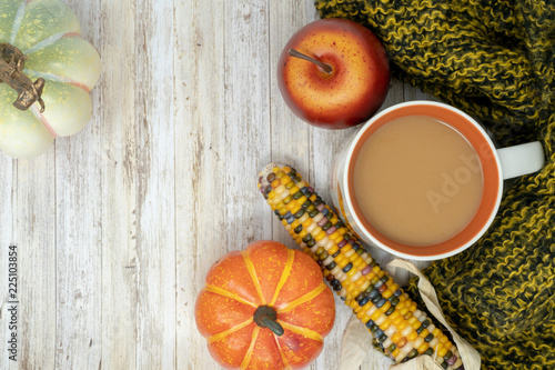 Cozy fall autumn background with coffee cup, indian corn, pumpkins, apple and a warm blanket. Room for copy space on wood background