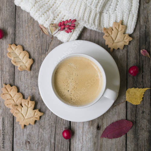 Coffee cup, knitted scarf, dry leaves, cookies, hawthorn and barberry fruitson a wooden background. Concept cozy atmosphere with a cup of coffee. Copy space, flat lay