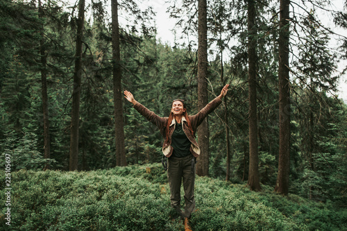 I am happy and free. Full length portrait of spirited young lady with closed eyes enjoying travel in the woods. She is spreading arms with joy and smiling