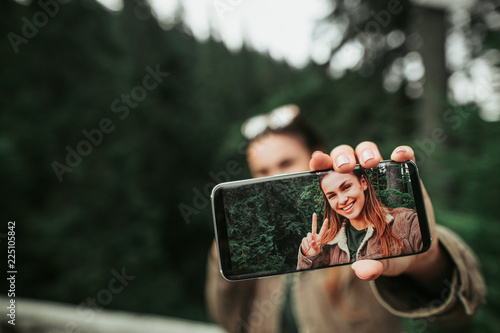 Look at me. Close up of mobile phone with photo of smiling girl in female hand. Woman and green forest on blurred background photo