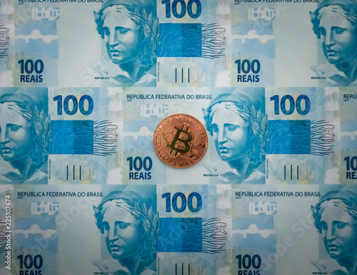 Criptomoeda Bitcoin bronze em cima de notas de cem reais © Hector