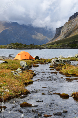 Russia, Arkhyz. The orange tent on the banks of Zaprudnoye lake in cloudy autumn day