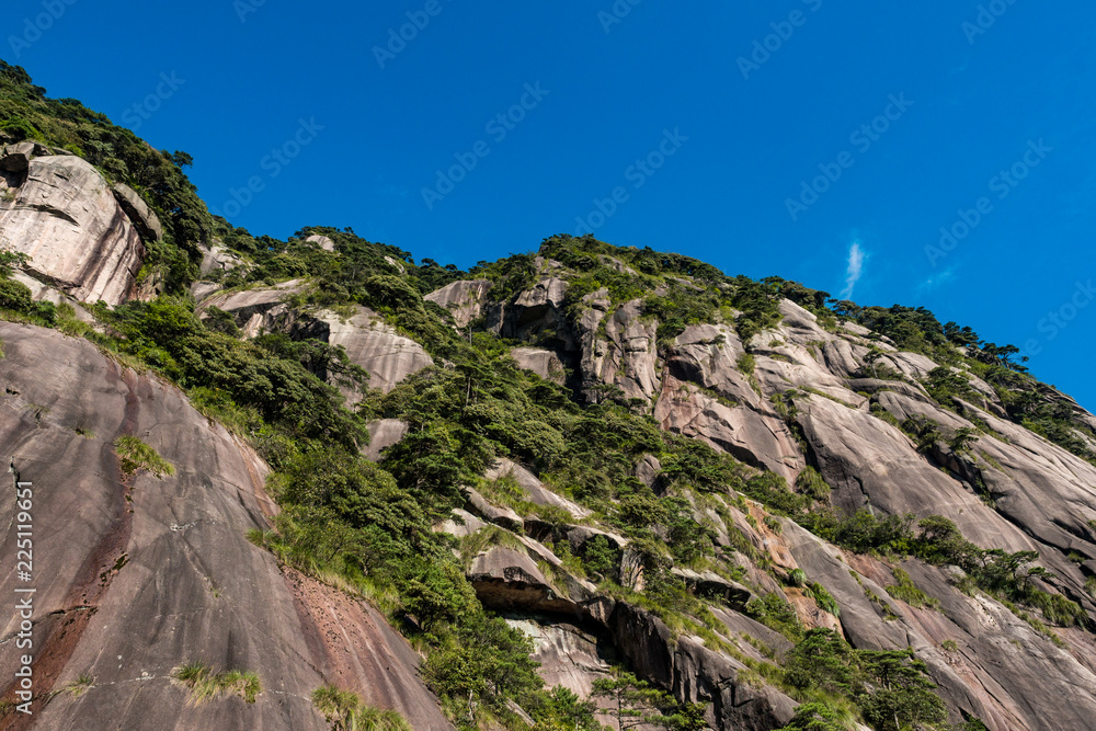 rock face on the mountain top covered in green on a sunny day under blue sky