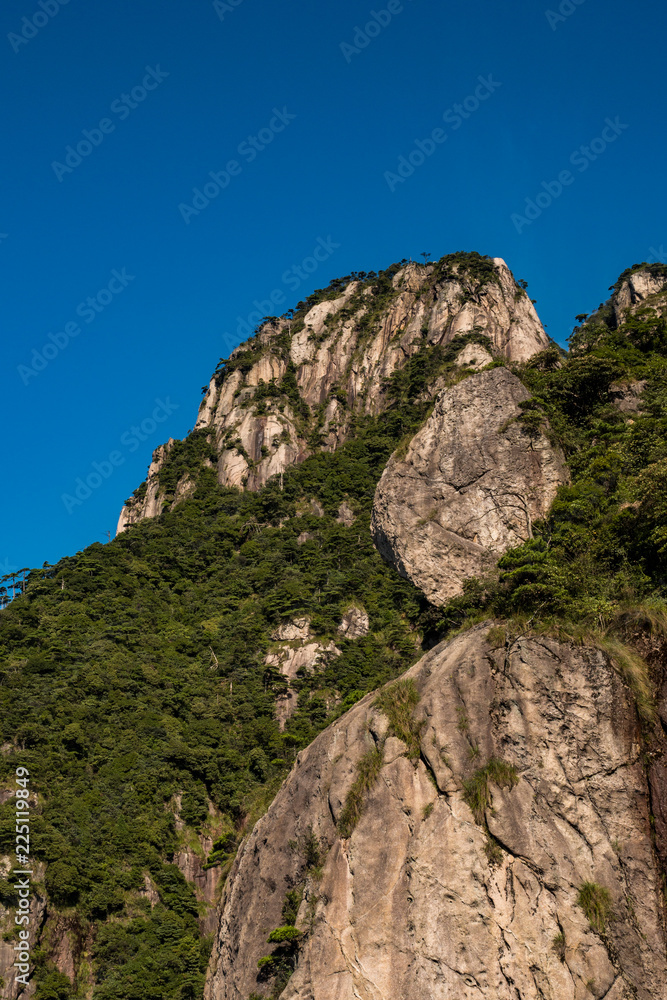 close up of unique peaks of Mt. SanQiang covered in green under cloudy blue sky close up of unique peaks of Mt. SanQiang covered in green under cloudy blue sky