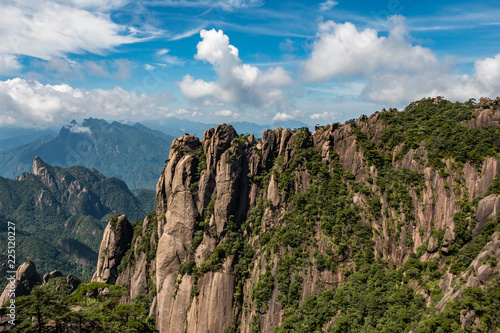 rock face on Mt. SanQiang covered with trees on a sunny day under the cloudy blue sky