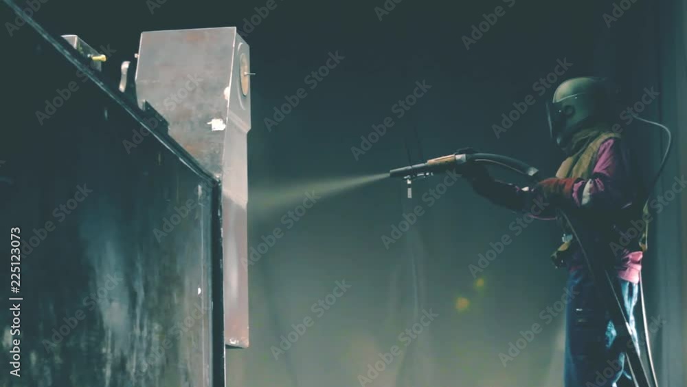 Man cleans metal surface by sandblaster gun in a metal construction factory. Shotblaster in a process