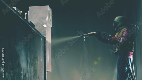 Man cleans metal surface by sandblaster gun in a metal construction factory. Shotblaster in a process