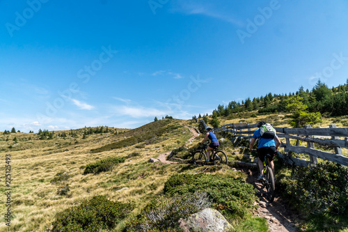 Zwei Mountainbiker auf schmalen Trail über Almwiese