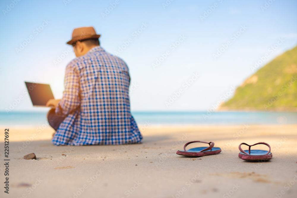 Selective focus,Young Asian man using laptop in blue shirt sitting on the beach,Freelancer working on sea beach background,copy space.