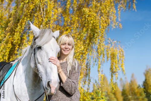Young blonde woman with a horse in autumn forest.