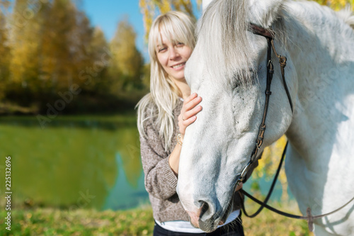 Beautiful blonde girl with a white horse posing in the autumn forest