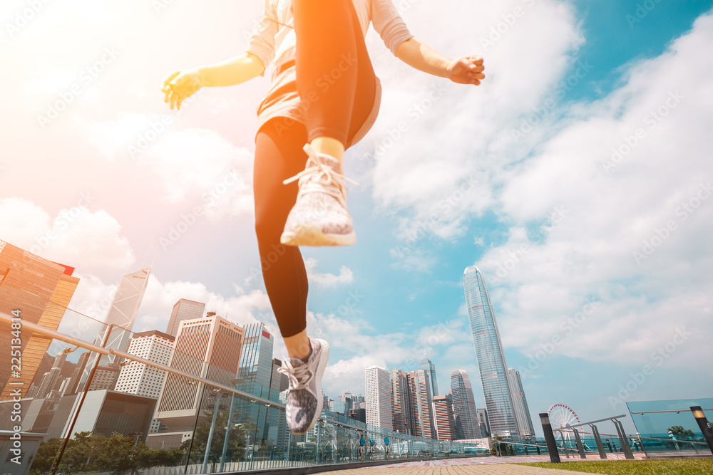 Woman runner jumping over the camera  with Hong Kong Cityscape in background - obrazy, fototapety, plakaty 