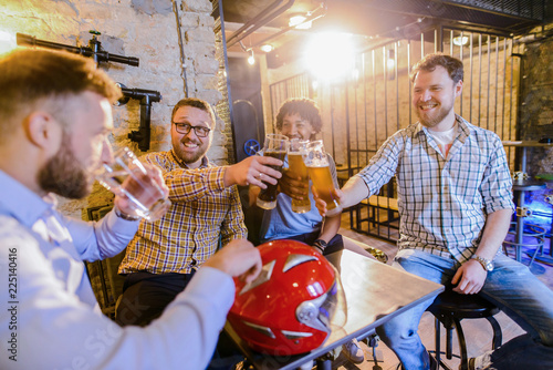 Male happy friends sitting in a bar and drinking beer. One man is drinking water while other are laughing to him.