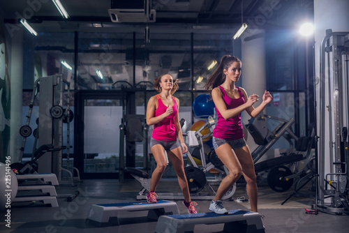 Two fit girl working out in a gym. Standing with one leg on stepper.