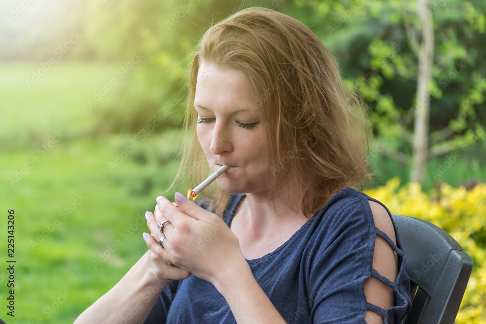 Portrait of a young woman lighting a cigarette outdoors in the garden. Portrait of a young woman lighting a cigarette outdoors in the garden.