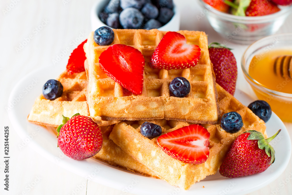 Photo of fresh homemade food made of berry Belgian waffles with honey, chocolate, strawberry, blueberry, maple syrup and cream. Healthy dessert breakfast concept with juice. Photo of fresh homemade food made of berry Belgian waffles with honey, chocolate, strawberry, blueberry, maple syrup and cream. Healthy dessert breakfast concept with juice.