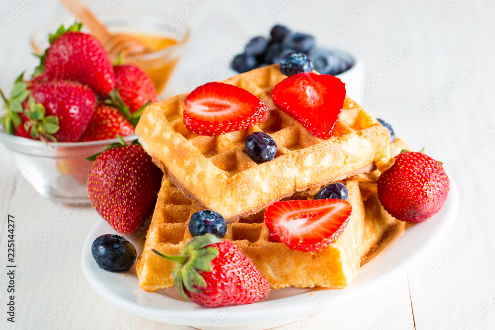 Photo of fresh homemade food made of berry Belgian waffles with honey, chocolate, strawberry, blueberry, maple syrup and cream. Healthy dessert breakfast concept with juice. Photo of fresh homemade food made of berry Belgian waffles with honey, chocolate, strawberry, blueberry, maple syrup and cream. Healthy dessert breakfast concept with juice.