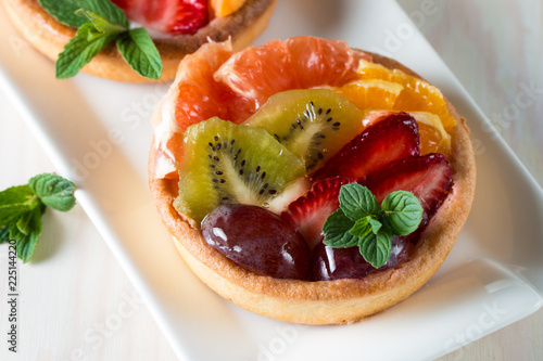 Fresh fruit and berry tart dessert with toss sugar on wooden background. Delicious sweet cake with raspberries, grapes, strawberries, cherry, kiwi, grapefruit and cream.