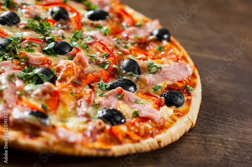 Pizza with Mozzarella cheese, ham, pepper, meat, Tomatoes, olives, Spices and Fresh Basil. Italian pizza on wooden background