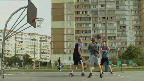 Active teenage friends playing two on two streetball game on outdoor basketball court. Young basketball player scoring field goal with layup shot after assist from his teammate during game outdoors.