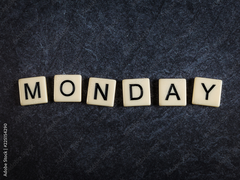 Scrabble letter tiles on black slate background spelling Monday Scrabble letter tiles on black slate background spelling Monday