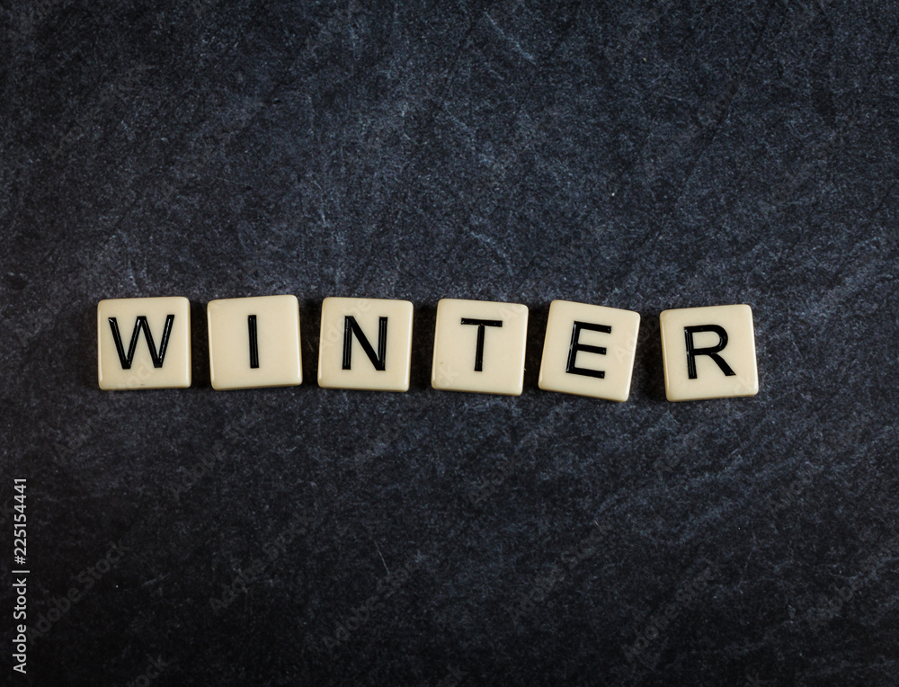 Scrabble letter tiles on black slate background spelling Winter Scrabble letter tiles on black slate background spelling Winter