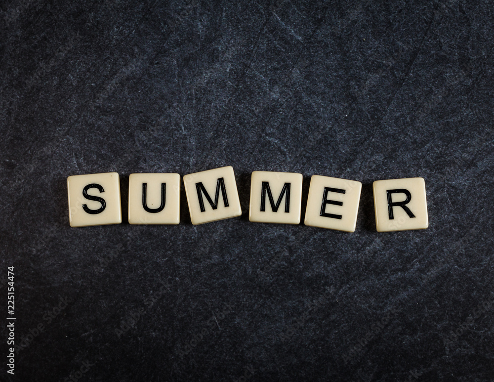 Scrabble letter tiles on black slate background spelling Summer Scrabble letter tiles on black slate background spelling Summer