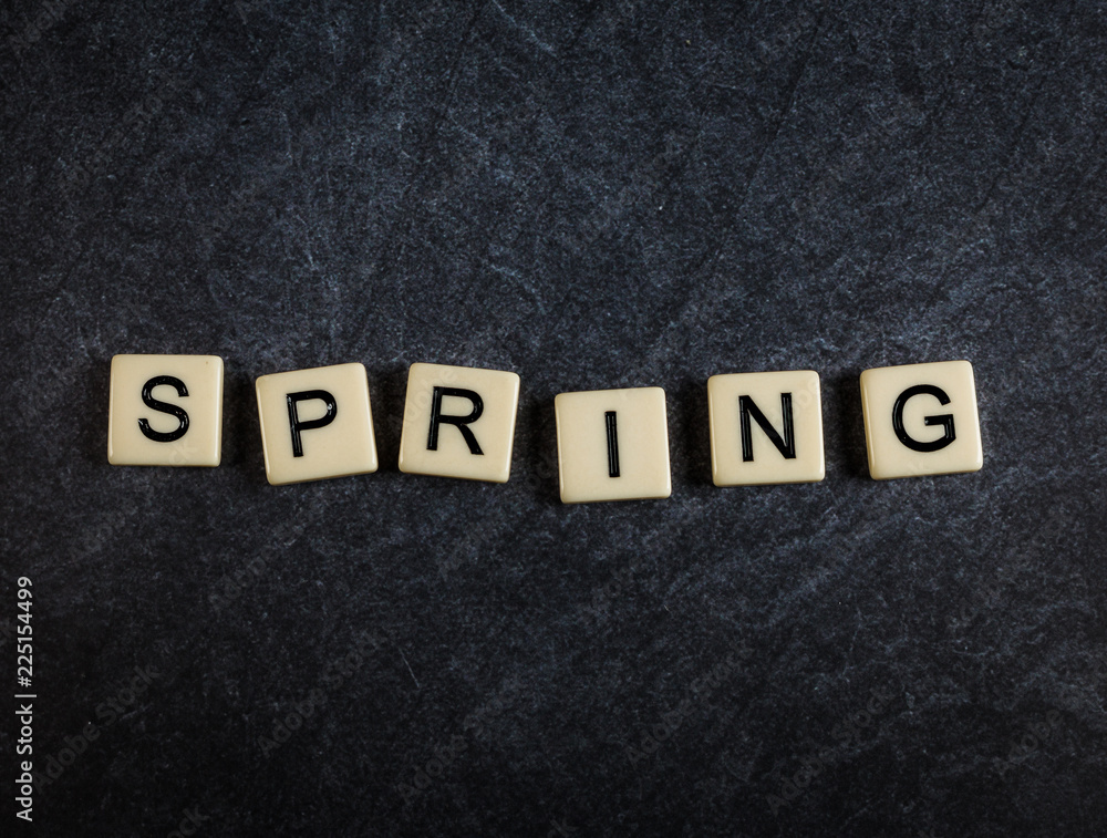 Scrabble letter tiles on black slate background spelling Spring Scrabble letter tiles on black slate background spelling Spring