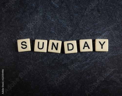 Scrabble letter tiles on black slate background spelling Sunday