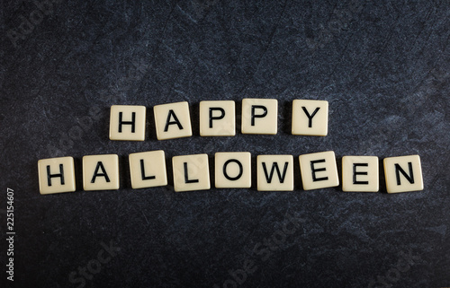 Scrabble letter tiles on black slate background spelling Happy Halloween