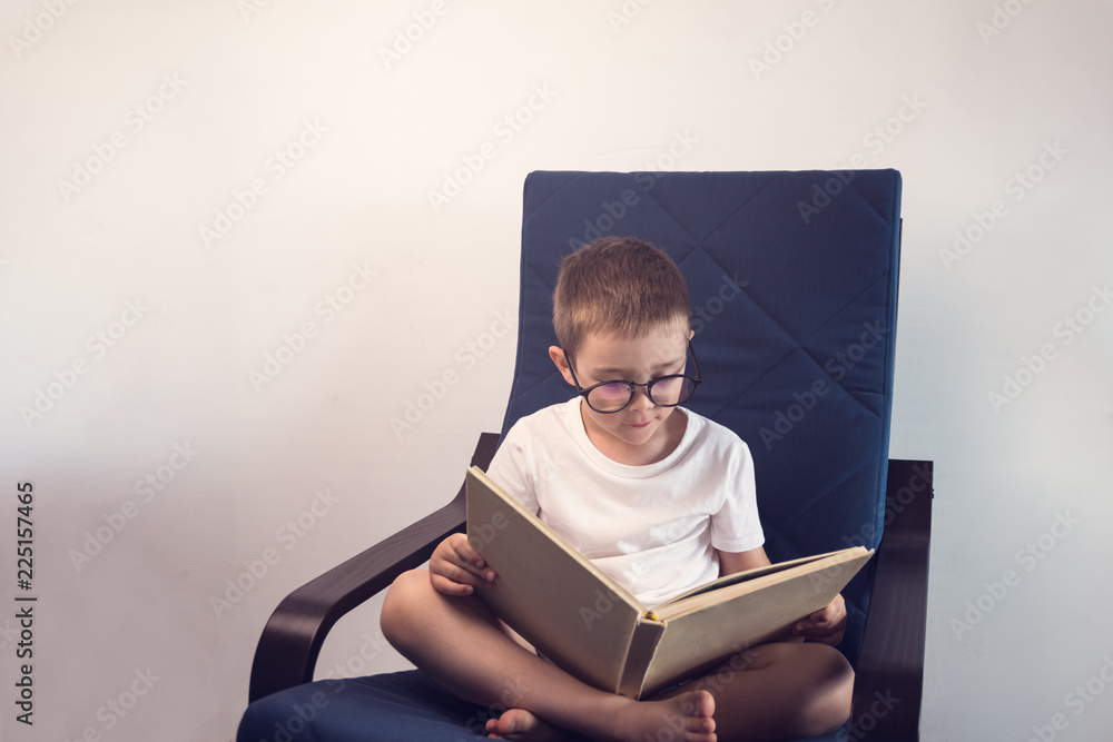 Obraz premium Young kid reading an interesting book sitting on the blue armchair. Concept of reading an interesting and exciting book everywhere.